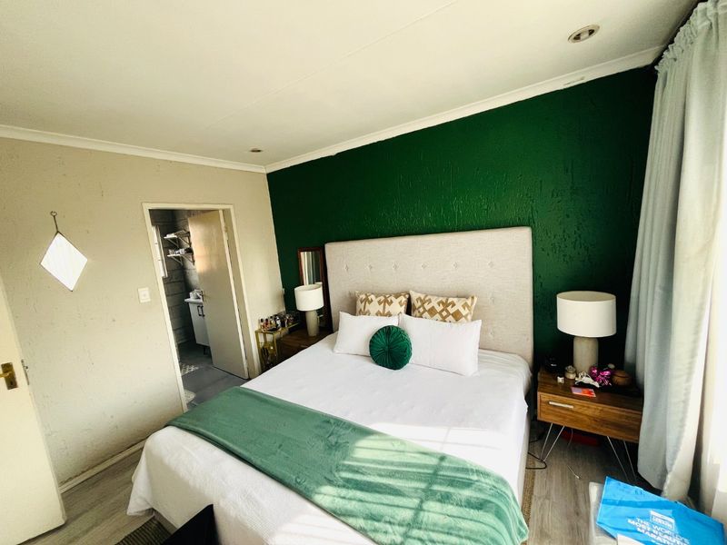 A bedroom featuring a bold green accent wall, recessed lighting, and laminate flooring, with an adjoining space visible through the doorway.