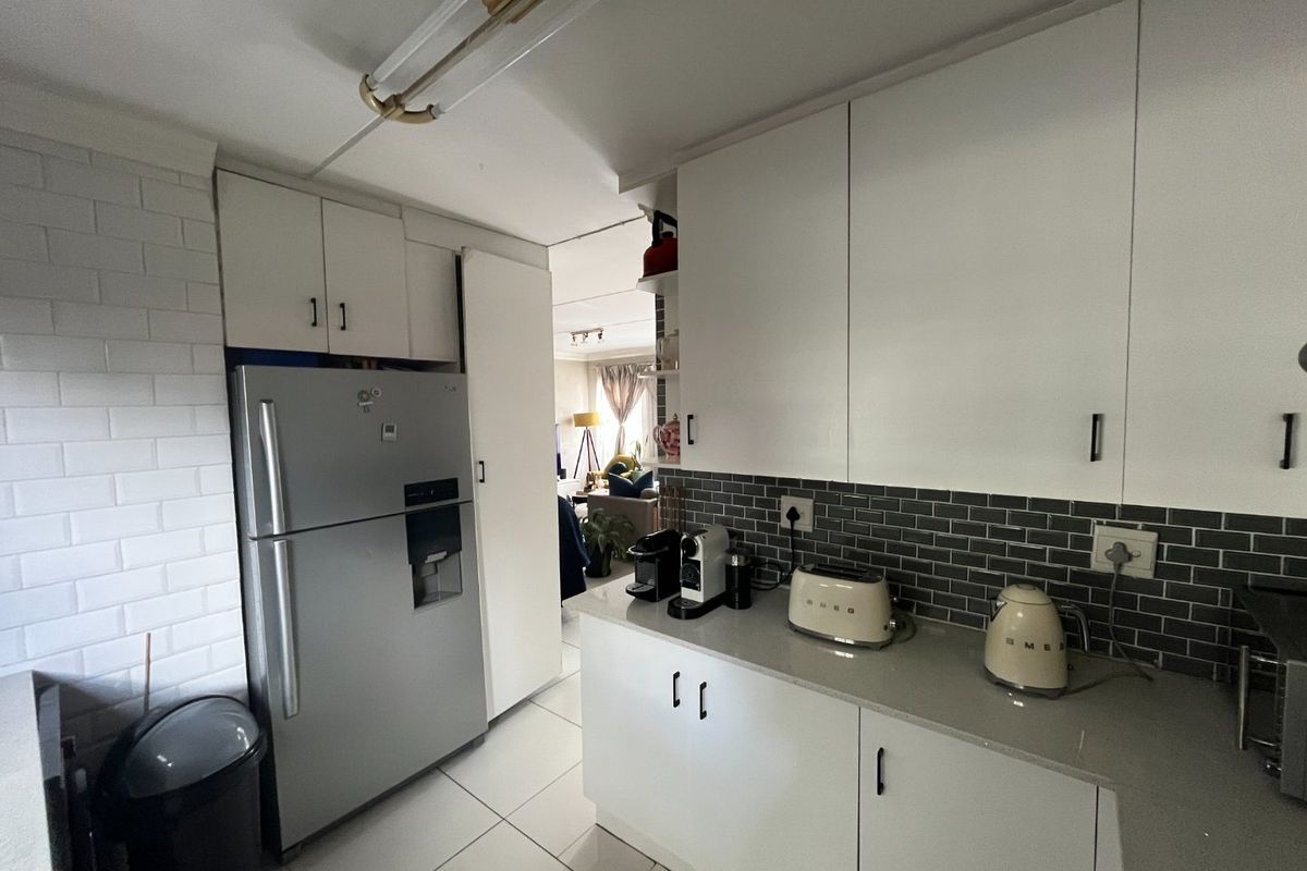 A functional kitchen featuring white cabinetry, grey subway tile backsplash, stone countertops, and tiled flooring, with a view leading into the living area.