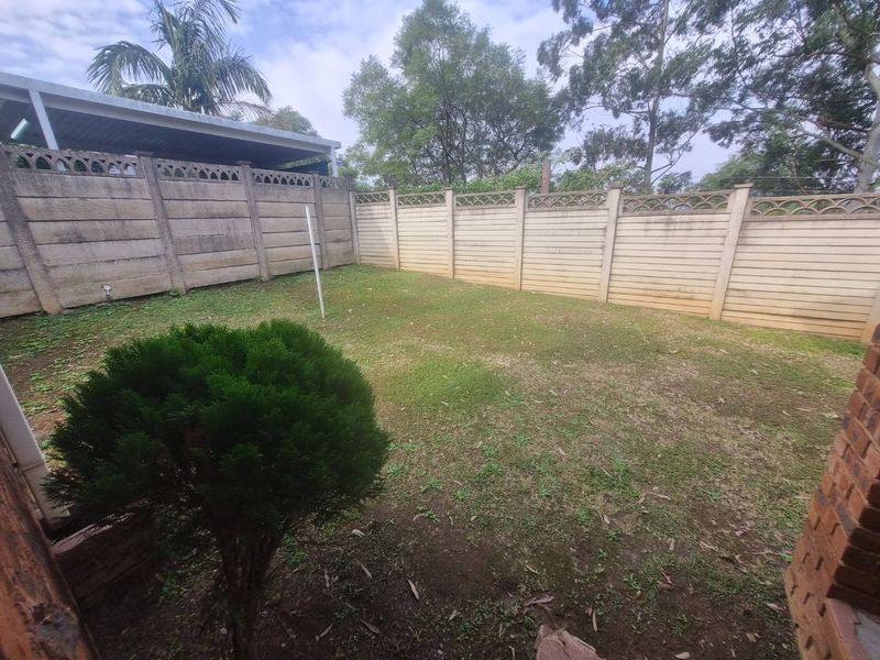 A private rear garden area featuring a lawn enclosed by precast concrete boundary walls and adjacent to a carport structure.
