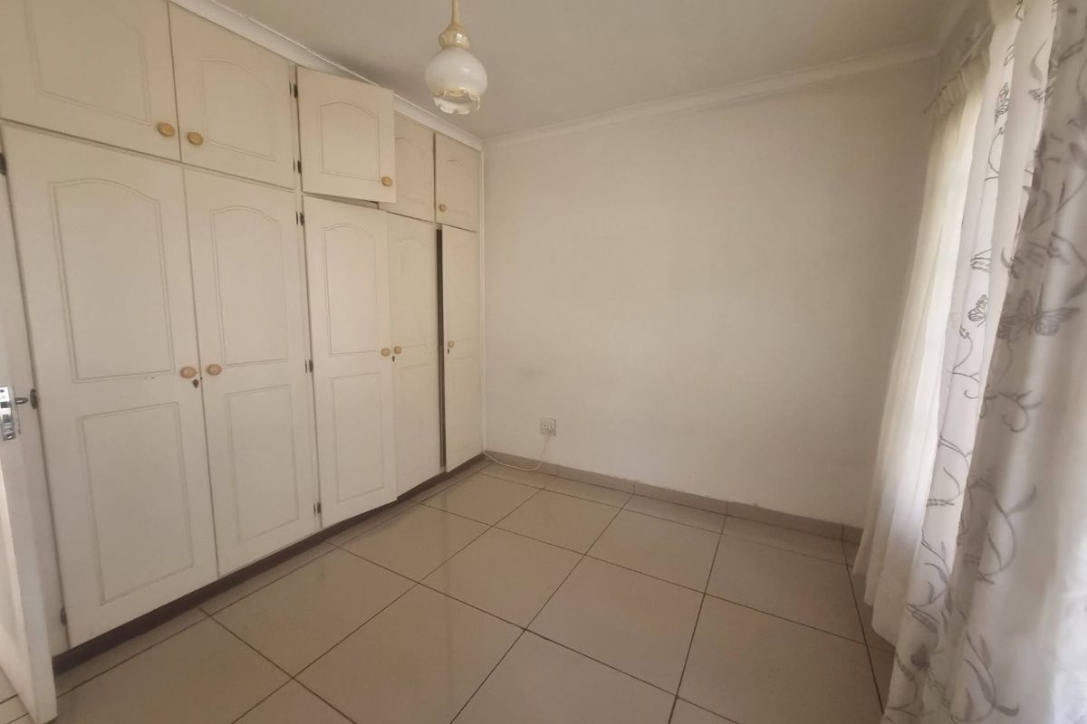 A bright, empty bedroom featuring neutral tiled flooring and extensive built-in cupboard storage with overhead cabinetry.