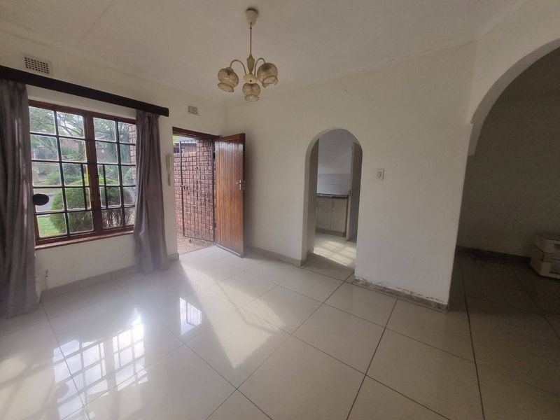 An empty living room featuring tiled flooring, an arched entryway, and a timber window frame, offering a bright and neutral space for potential styling.