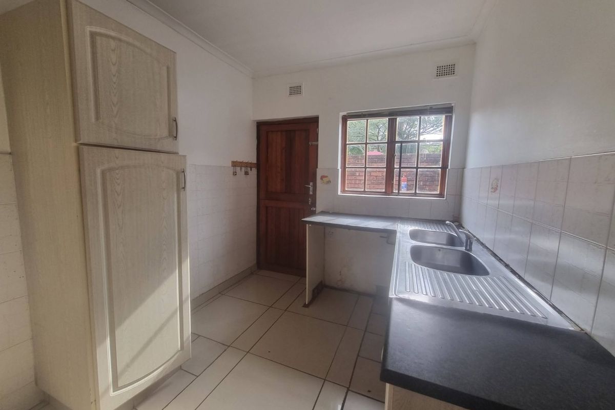 A functional, empty kitchen featuring built-in cabinetry, a double stainless steel sink, tiled flooring, and a rear timber door leading outside.