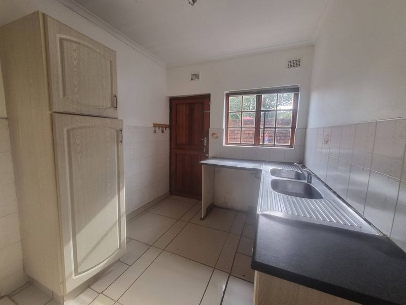 A functional, empty kitchen featuring built-in cabinetry, a double stainless steel sink, tiled flooring, and a rear timber door leading outside.