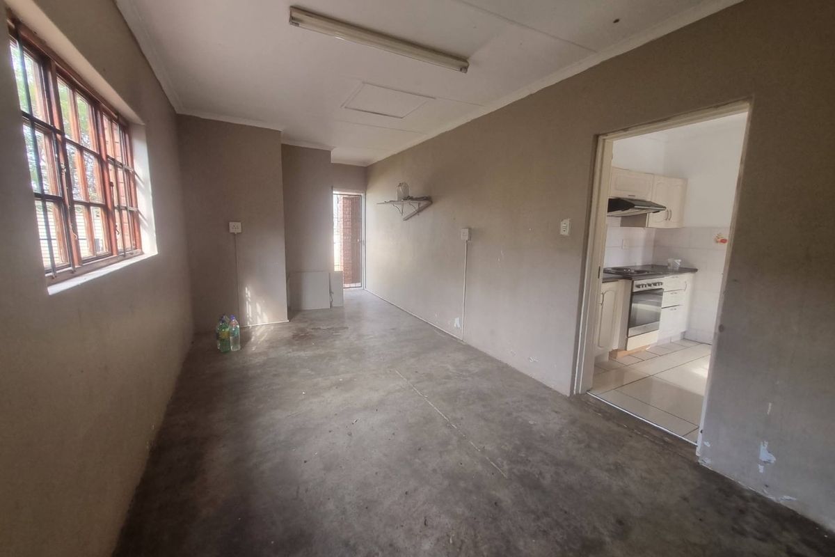 An empty living area with concrete flooring and steel-framed windows, leading into a separate kitchen space.