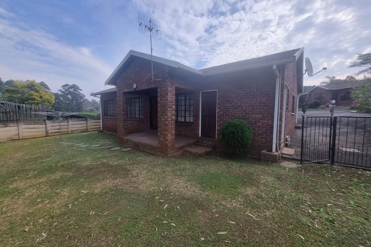 Rear view of a face-brick townhouse featuring a covered patio, lawn area, and secure boundary fencing.