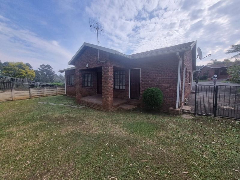 Rear view of a face-brick townhouse featuring a covered patio, lawn area, and secure boundary fencing.