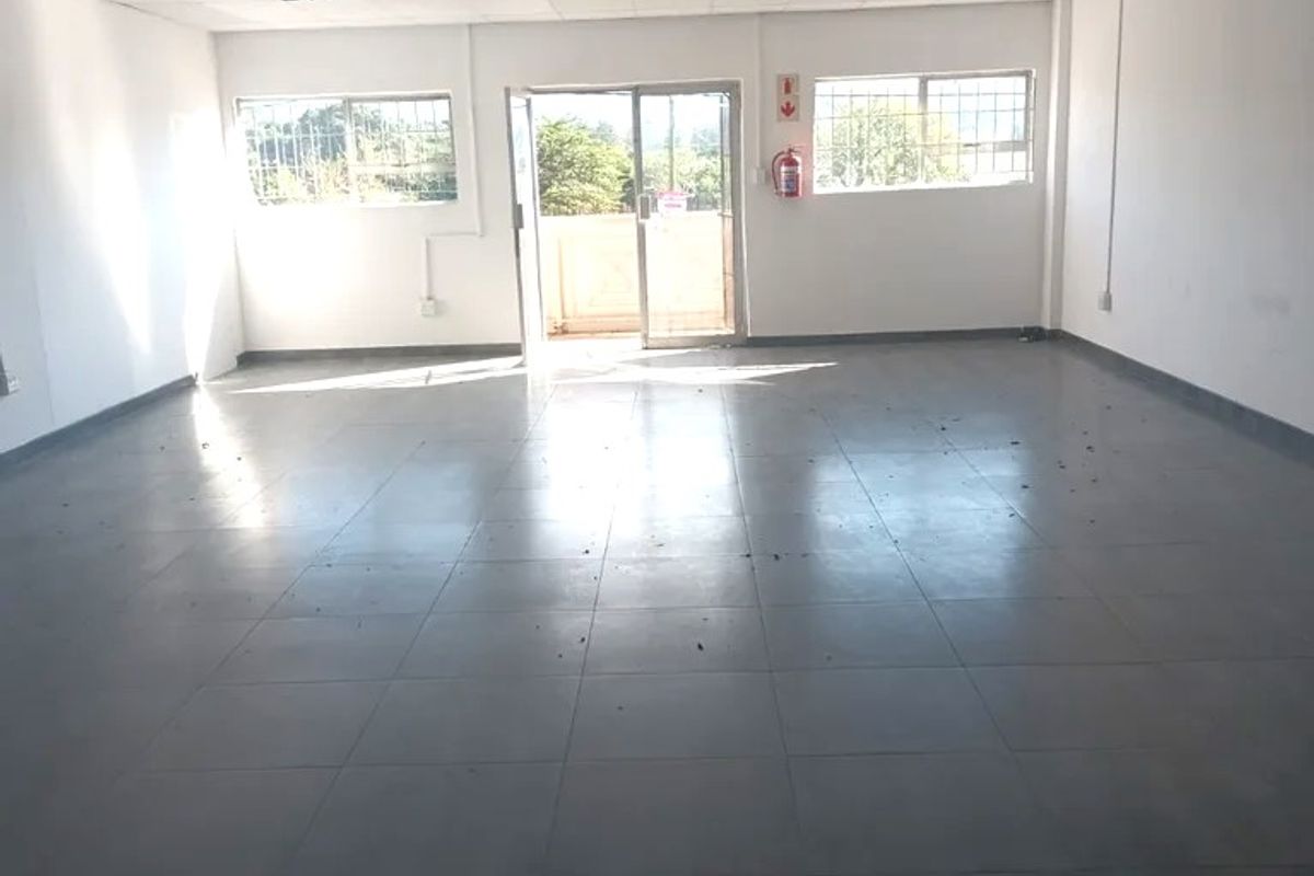An empty, open-plan commercial office space featuring tiled flooring, a suspended ceiling with recessed lighting, and access to an exterior balcony.
