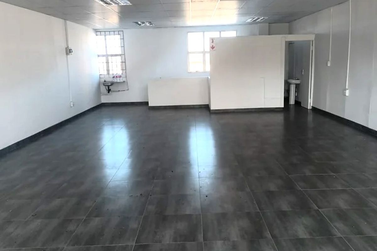A spacious, open-plan commercial office area featuring tiled flooring, a suspended ceiling with recessed lighting, and a small partitioned section with a wash basin.