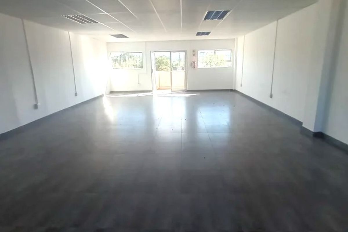 A spacious, empty open-plan commercial office area featuring tiled flooring, a suspended ceiling with recessed lighting, and a sliding glass door entrance.