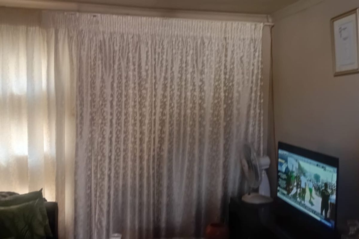 A living room area featuring a wall-mounted extractor fan and large window coverings.