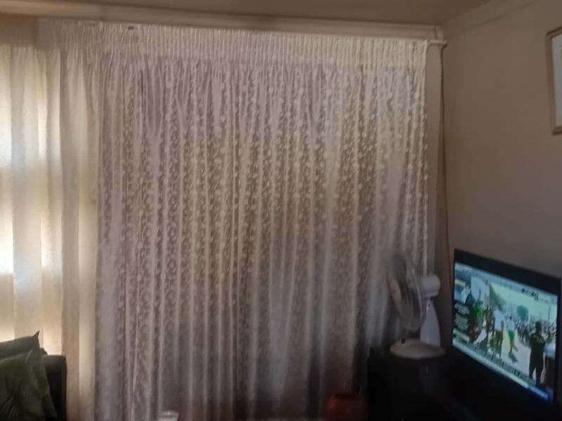 A living room area featuring a wall-mounted extractor fan and large window coverings.