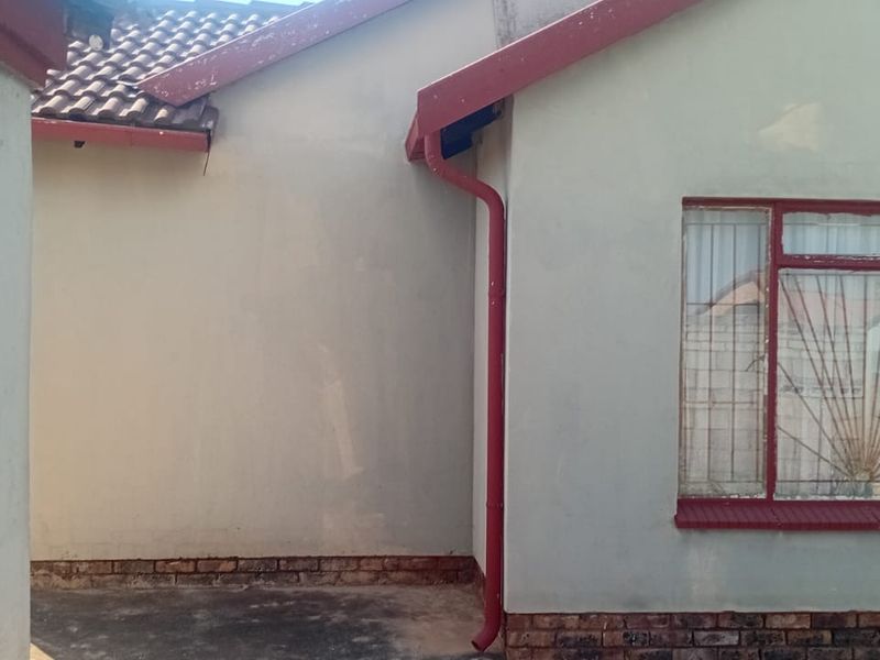 Front elevation of a residential house featuring a tiled roof, red metal window frames, and a brick plinth base.
