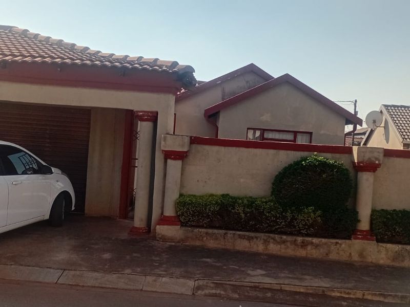 Front elevation of a residential house featuring a tiled roof, integrated garage, and a boundary wall with established garden hedging.