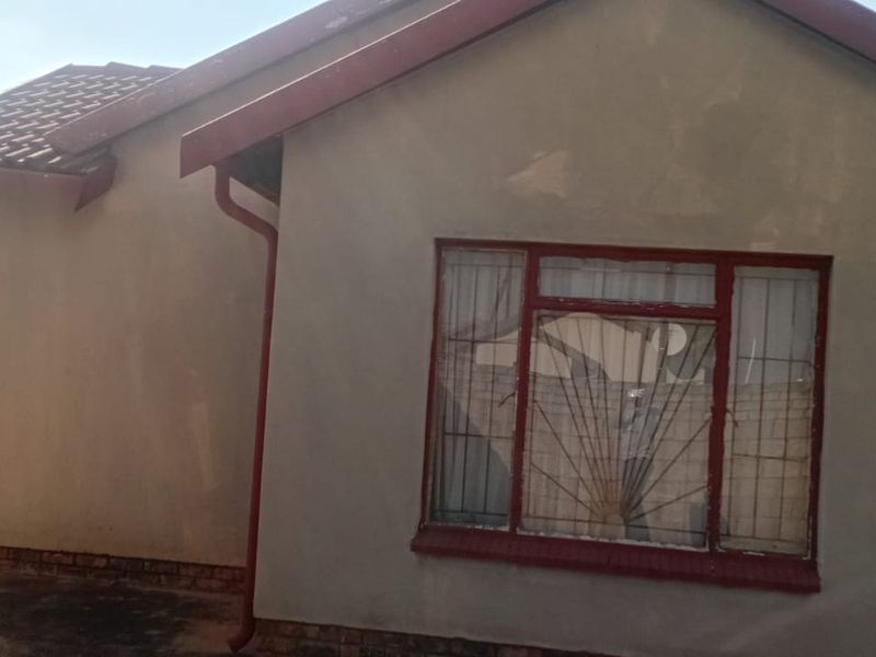 Rear view of the property featuring a tiled roof, gutters, and security bars on the windows, with visible wear to the exterior plaster.
