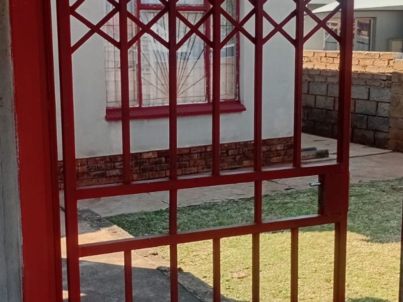 View of the rear yard featuring a red security gate, concrete paving, and a brick boundary wall.