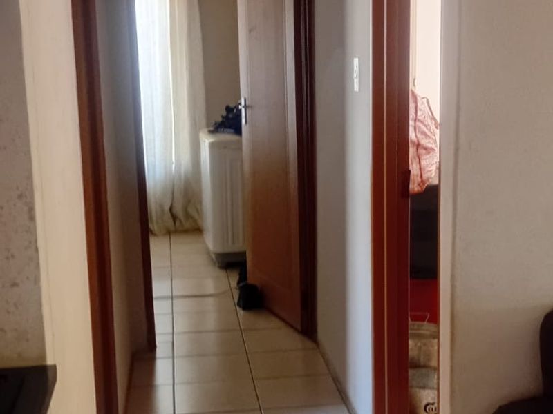 A narrow residential hallway featuring tiled flooring, wooden door frames, and a ceiling access hatch, connecting multiple rooms within the home.