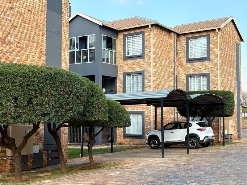 Exterior view of a multi-story apartment complex featuring face brick construction, covered parking bays, and well-maintained landscaped grounds.