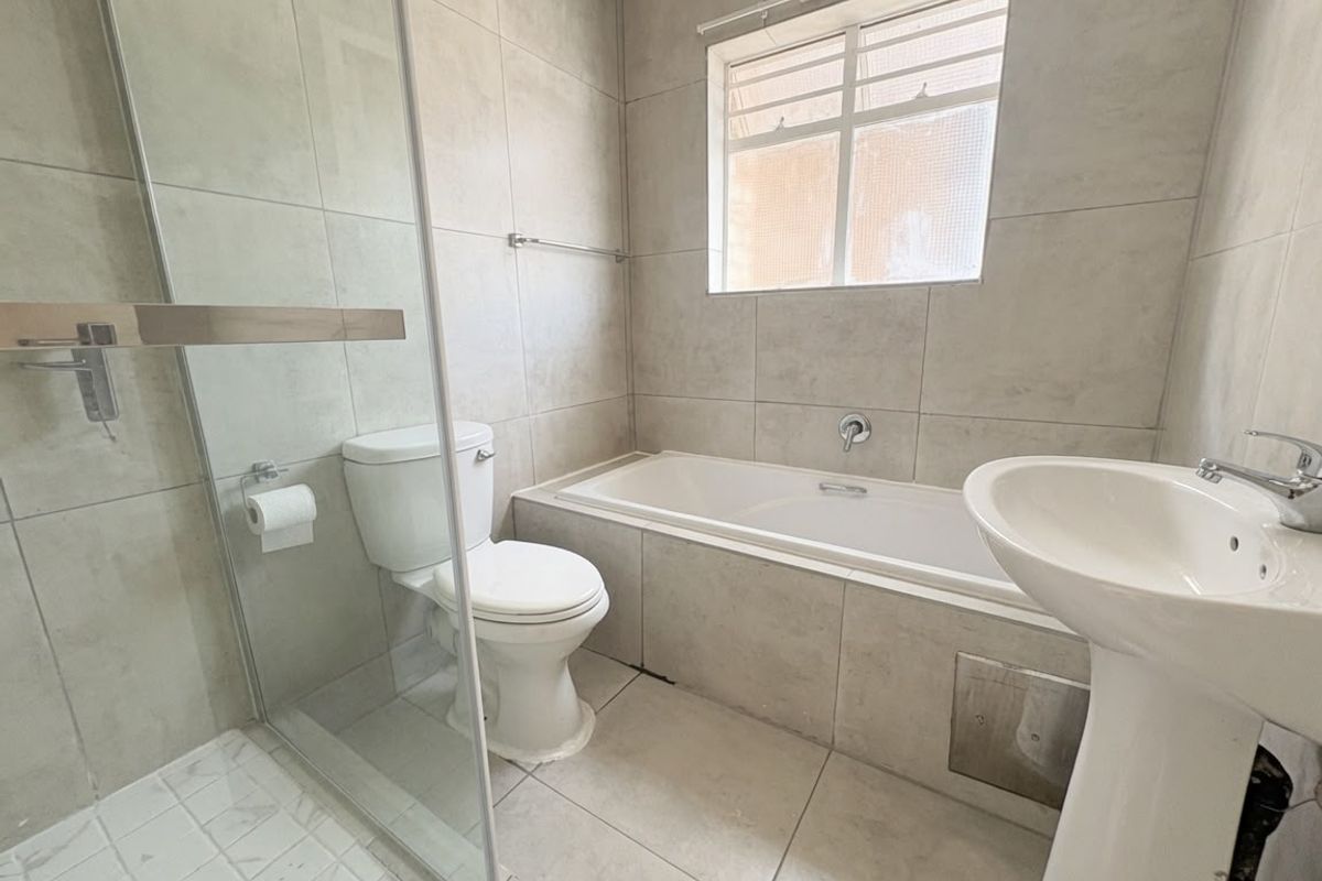 A functional bathroom featuring a glass-enclosed shower, a built-in bathtub, and a pedestal basin with neutral wall and floor tiling.