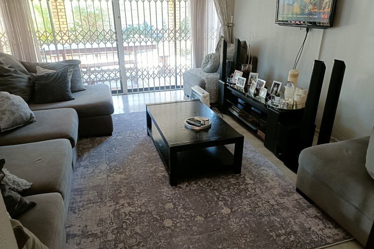 A comfortable living room featuring tiled flooring and a large sliding glass door with a security gate leading to the outdoor area.