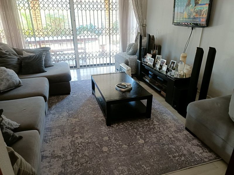 A comfortable living room featuring tiled flooring and a large sliding glass door with a security gate leading to the outdoor area.