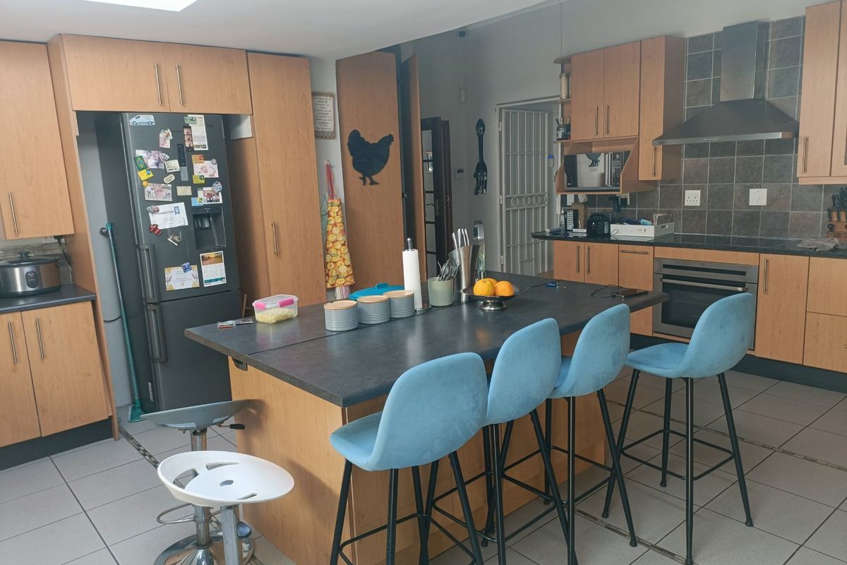 A functional kitchen featuring wood-finish cabinetry, a central island with seating, built-in oven, extractor fan, and tiled flooring with natural light from a skylight.