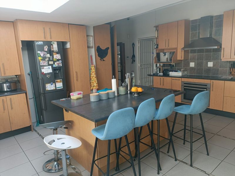 A functional kitchen featuring wood-finish cabinetry, a central island with seating, built-in oven, extractor fan, and tiled flooring with natural light from a skylight.