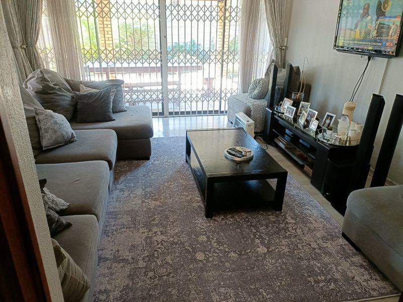 A comfortable living room featuring tiled flooring and a large sliding glass door with a security gate leading to the outdoor area.