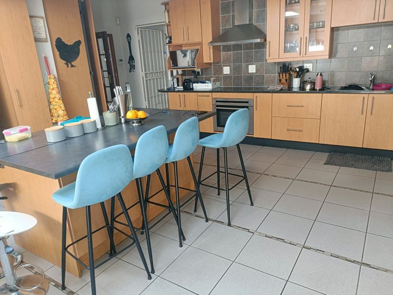 A functional kitchen featuring wooden cabinetry, a central island with breakfast bar seating, tiled flooring, and integrated cooking appliances.