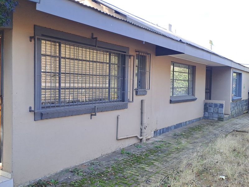 Rear exterior view of the house featuring paved walkways, security bars on windows, and stone cladding accents along the base of the wall.