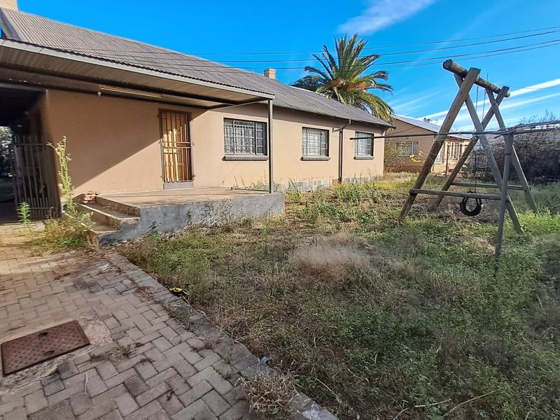 Rear view of the property featuring a covered patio, paved walkway, and an expansive garden area with established landscaping.