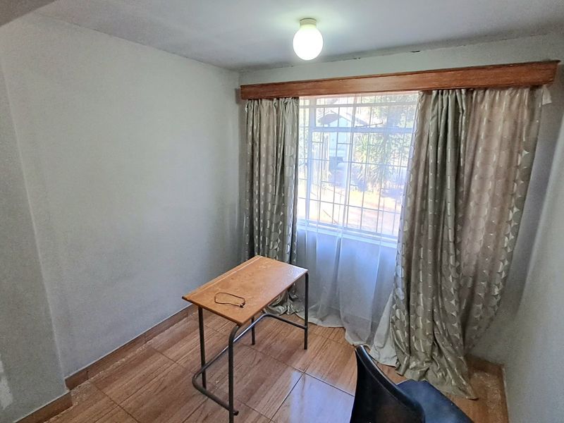 A bedroom featuring tiled flooring and window security bars, currently requiring finishing touches to the wall surfaces.