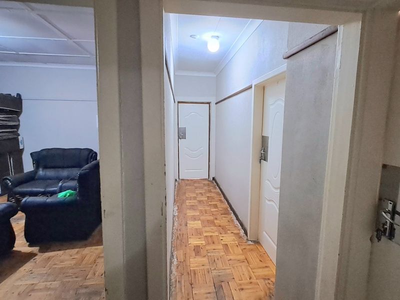 A narrow hallway featuring parquet flooring and moulded interior doors, leading into an adjacent living area with similar flooring.
