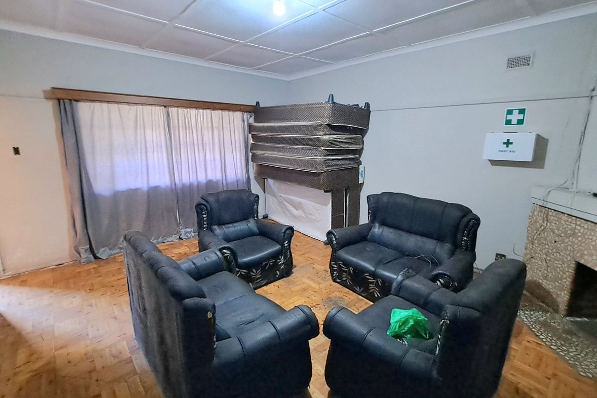 A living room featuring parquet flooring and a stone-clad fireplace, offering a dated interior space with potential for renovation and modernization.