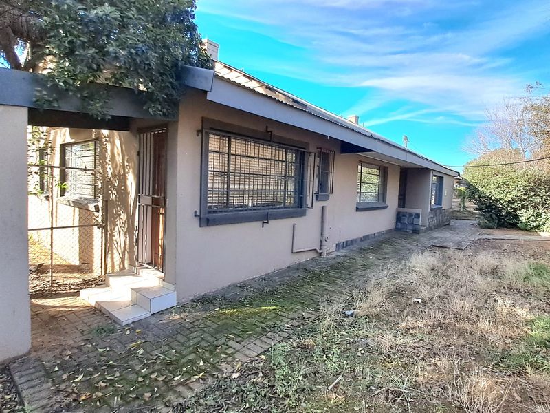 Rear exterior view of the house featuring a paved walkway, security bars on windows, and a covered entrance area with tiled steps.