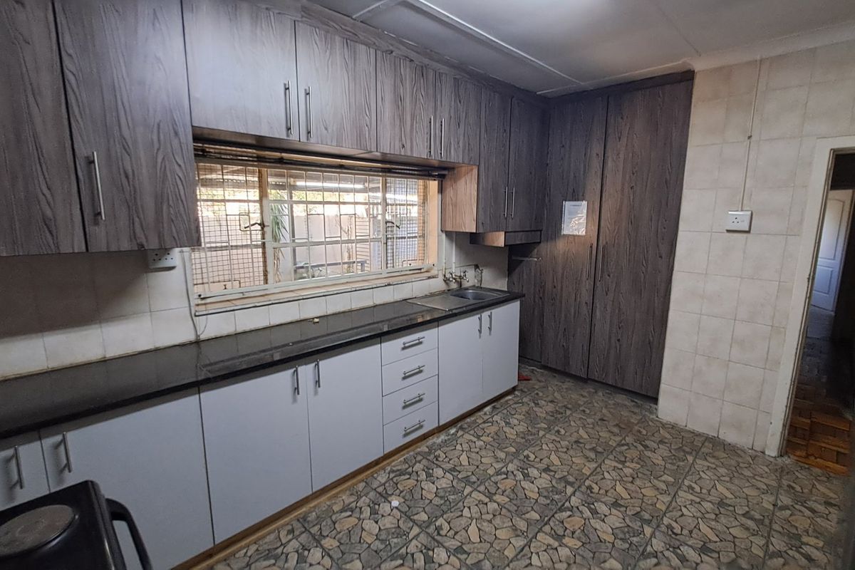 A functional kitchen featuring dark wood-look upper cabinetry, light lower cabinets, granite countertops, and a stainless steel sink with security-barred window.