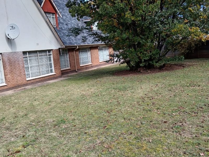 A view of the rear garden and the side elevation of the house, featuring a tiled roof, brick exterior, and security bars on the windows.