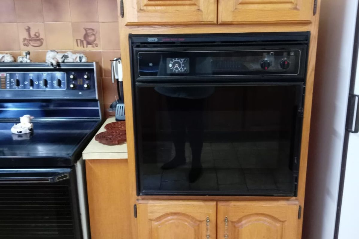 A dated kitchen featuring wooden cabinetry, a built-in oven, an extractor fan, and tiled splashbacks with ceramic floor tiles.