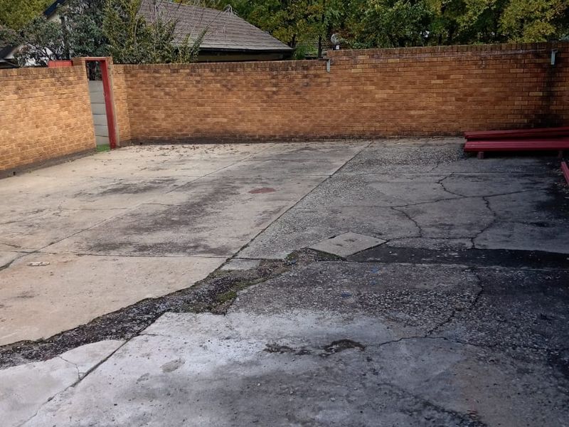 A spacious rear outdoor area featuring a brick boundary wall and extensive concrete paving in need of repair and maintenance.