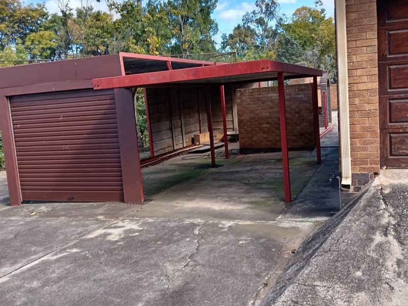 Exterior view of a detached metal carport and garage structure with a weathered finish and cracked concrete driveway.