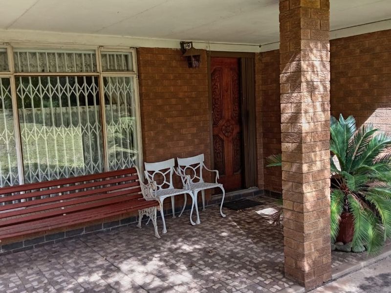 Covered front patio area featuring brick pillar support, tiled flooring, and a decorative timber entrance door.