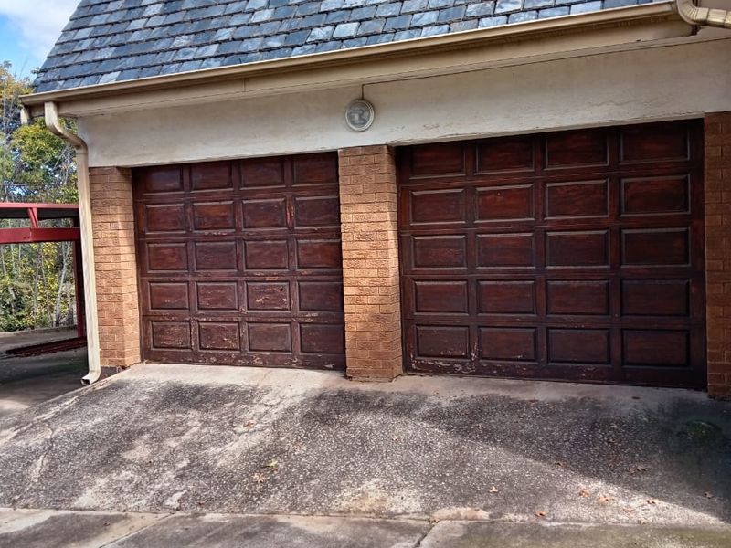 A double garage with a slate roof and brick facade, featuring weathered wooden doors and a concrete driveway showing signs of wear.