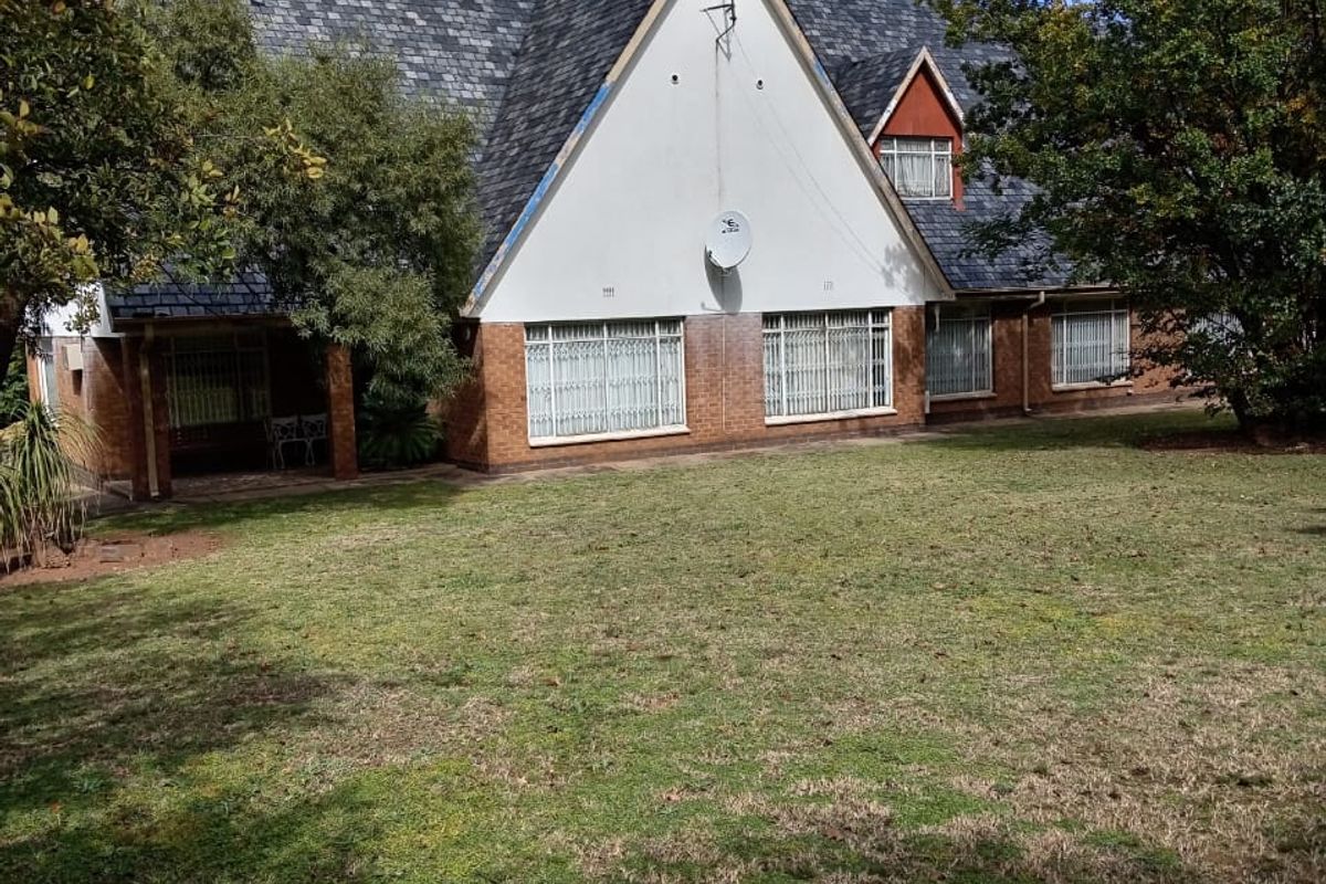 Rear view of a traditional house featuring a steep slate roof, brick lower walls, and a large garden area.