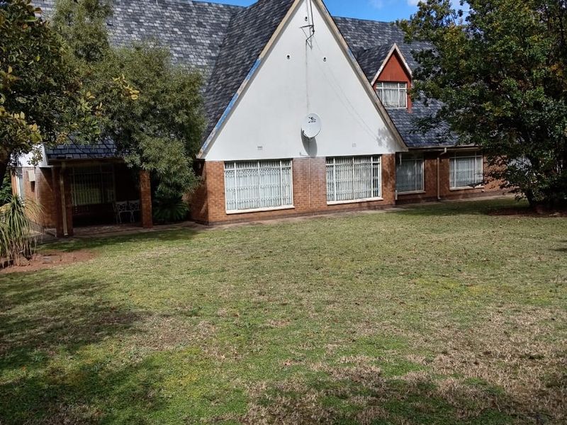 Rear view of a traditional house featuring a steep slate roof, brick lower walls, and a large garden area.