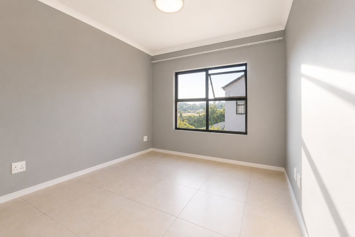 A bright, empty bedroom featuring neutral grey walls, tiled flooring, and a large window with a view.