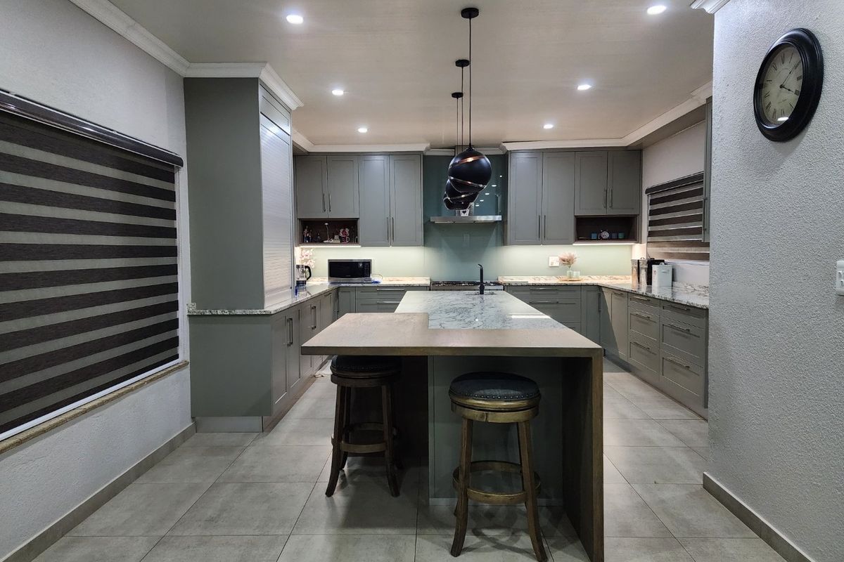 Modern kitchen featuring sage green cabinetry, a central island with stone countertops, integrated appliances, and contemporary pendant lighting.