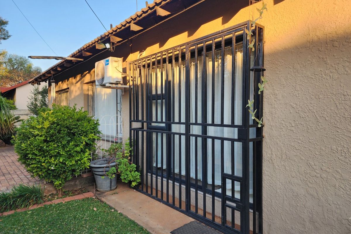 Rear exterior view of the property featuring a security gate, wall-mounted air conditioning unit, and a paved walkway alongside the building.