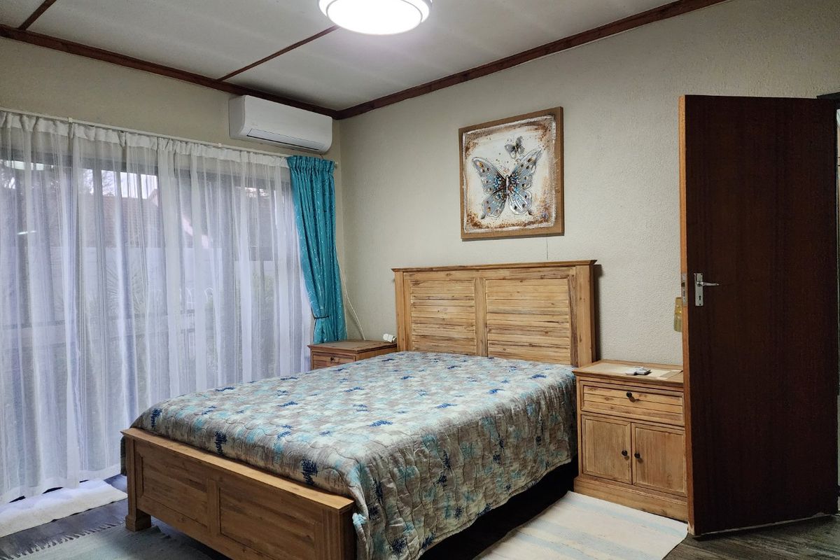 A functional bedroom featuring a split-system air conditioner, timber-framed ceiling details, and a sliding glass door providing access to the exterior.