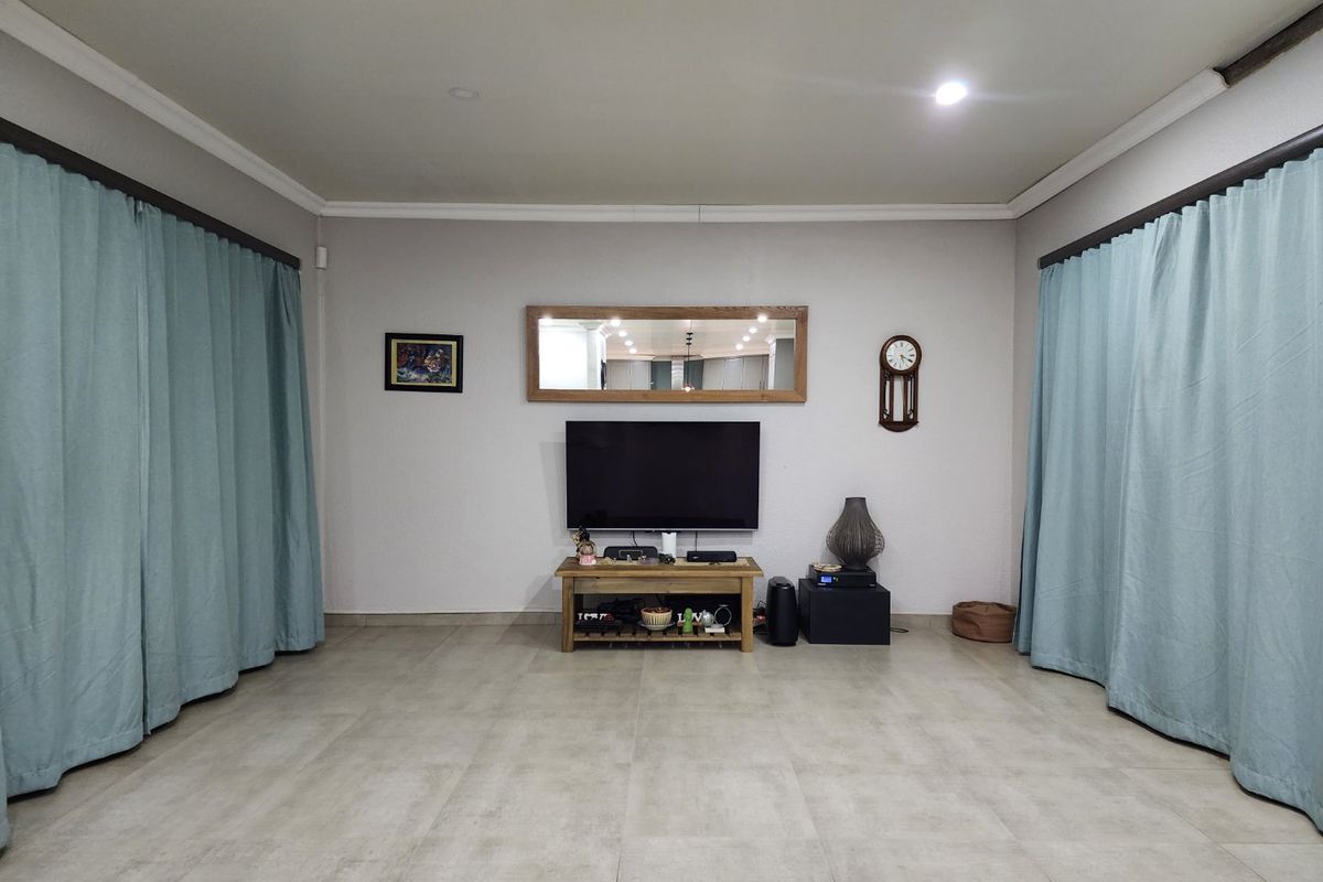A spacious living room featuring neutral tiled flooring, recessed downlighting, and decorative cove cornicing, providing a clean and versatile foundation for living space.