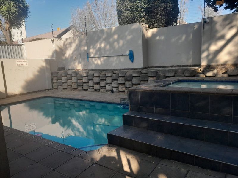 Outdoor pool area featuring a swimming pool with tiled steps, a retaining wall, and perimeter security fencing.