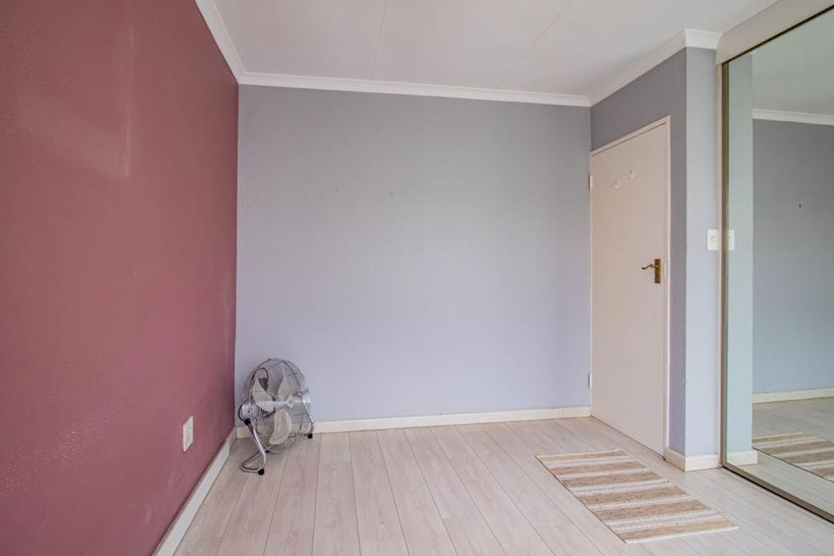 A bright, empty bedroom featuring light laminate flooring, a mirrored built-in wardrobe, and a neutral color palette with a feature wall.